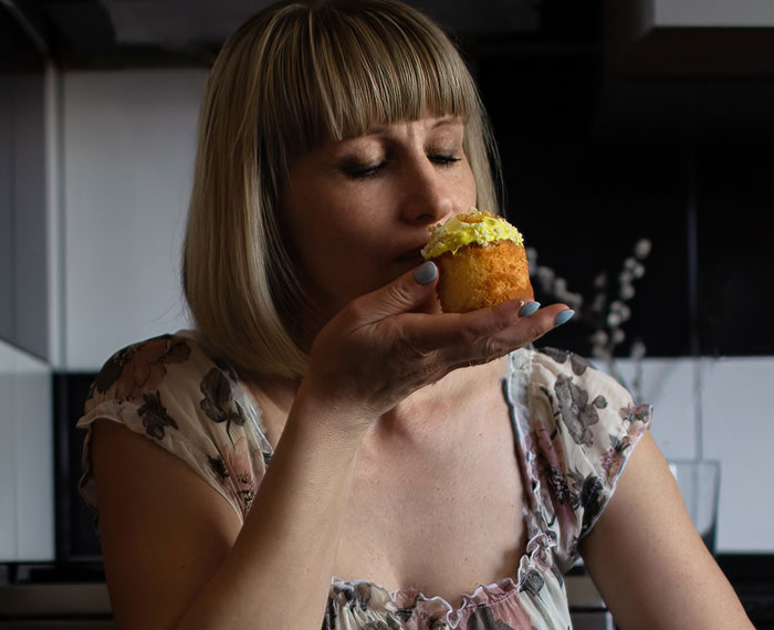 Pregnant woman holding a cupcake in a kitchen, eyes closed, savoring the treat. Pregnant woman holding a cupcake in a kitchen, eyes closed, savoring the treat.