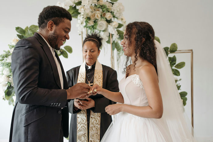Bride and groom exchanging rings at a wedding ceremony, bride considering last name impact on respect in community.