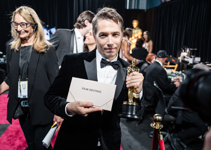 Winner holding Oscar for Film Editing, with a smile in a backstage setting at the Oscars 2025.