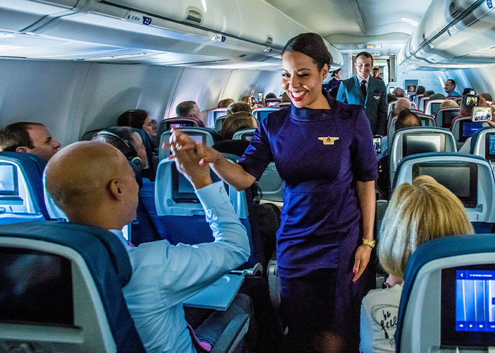 Flight attendant interacting with passengers in an airplane aisle, smiling and engaging in conversation. Flight attendant interacting with passengers in an airplane aisle, smiling and engaging in conversation.