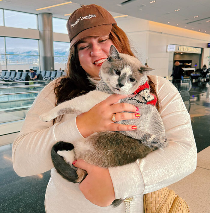 Pet parent holds a cat at the airport, smiling warmly. Pet parent holds a cat at the airport, smiling warmly.