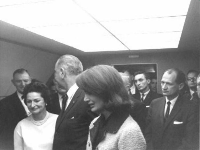 A black and white photo of formally dressed individuals in a room, capturing a moment with a dark history.