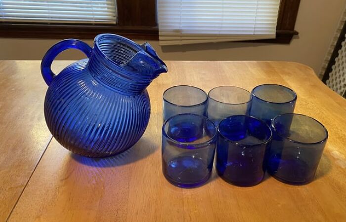 Vintage blue glass pitcher with six matching tumbler glasses on a wooden table.