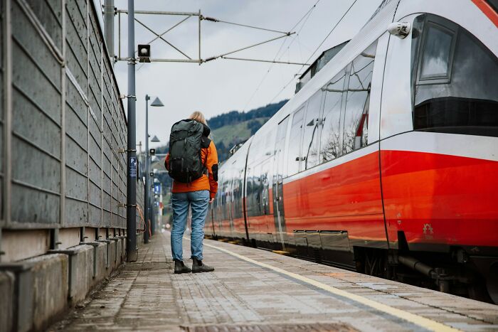 A person with a backpack stands on a train platform, facing the train, reflecting on personal secrets.