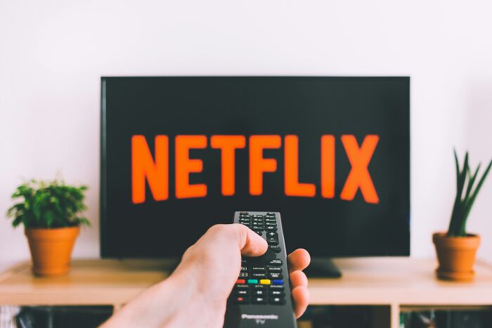 Remote in hand pointing at a TV screen displaying Netflix, suggesting simple approaches to enhance life quality.