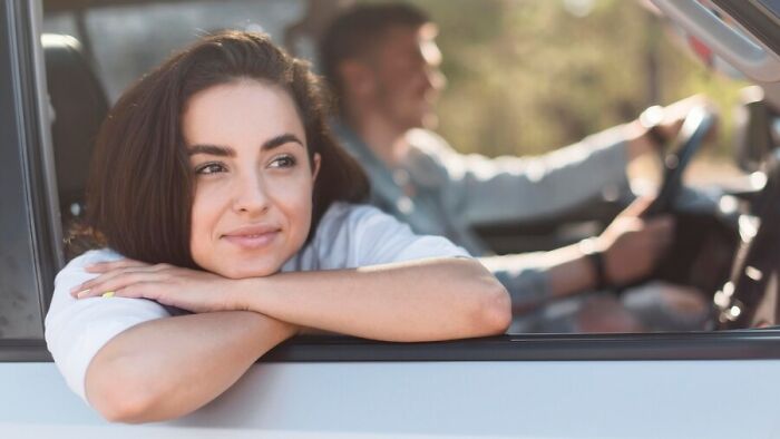 Woman smiling in car, a man driving, symbolizing unexpected guests and shared spaces.