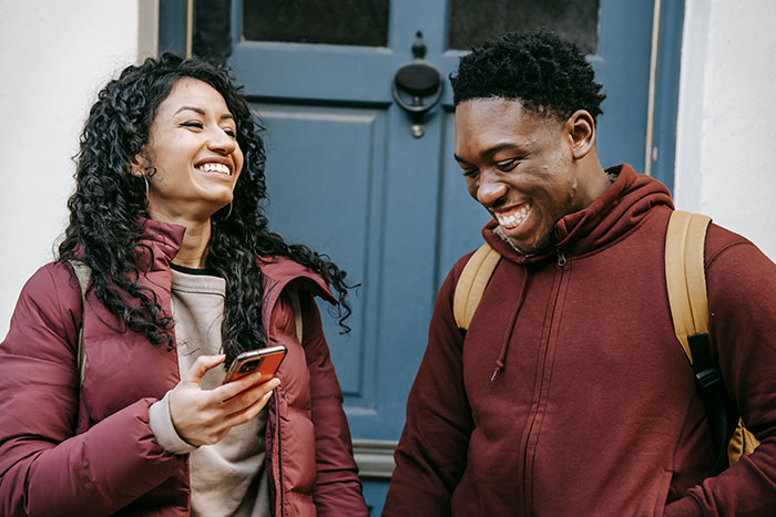 Two friends smiling and sharing a light moment outside a building, expressing friend regret and best friend confession. Two friends smiling and sharing a light moment outside a building, expressing friend regret and best friend confession.