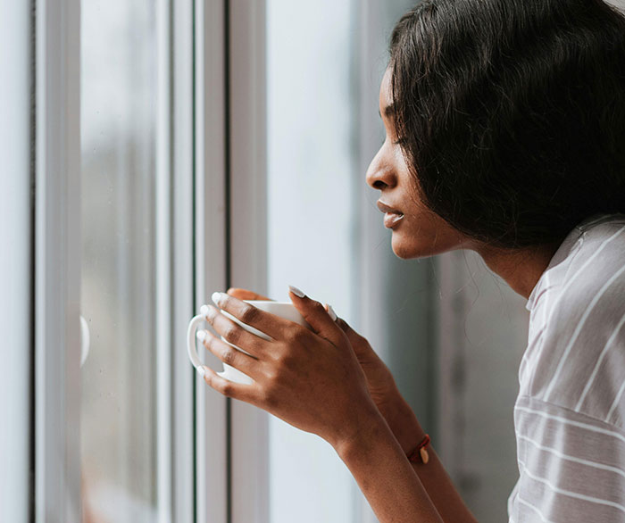 Young woman holding a cup and looking out the window, reflecting on friend regret and best friend confession feelings. Young woman holding a cup and looking out the window, reflecting on friend regret and best friend confession feelings.