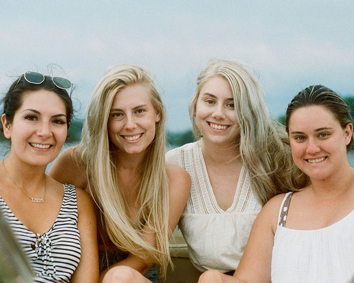 Four women smiling together on a boat during vacation, enjoying a child-free moment.