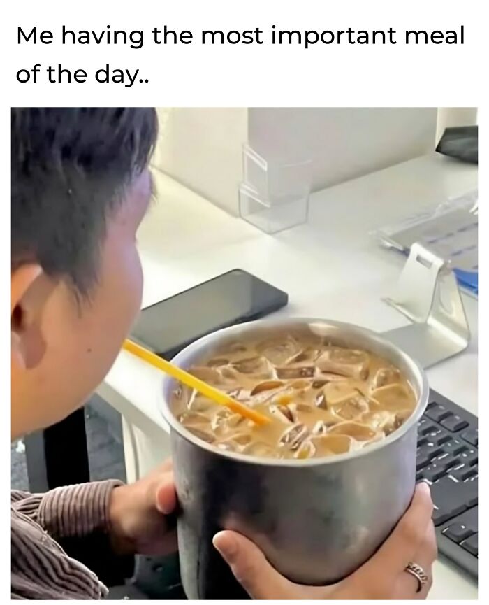 Person drinks iced coffee from a large mug at a desk, captioned “Me having the most important meal of the day.”
