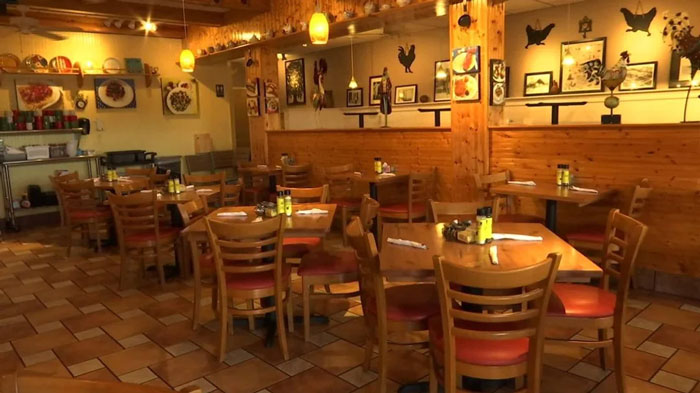 Empty restaurant with wooden decor, tables, and chairs, showcasing eclectic artwork on the walls.