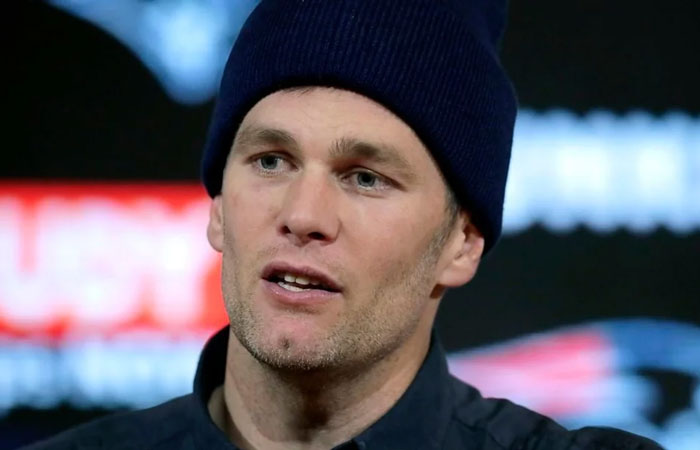 Man wearing a dark beanie and shirt, speaking in front of a blurred background.