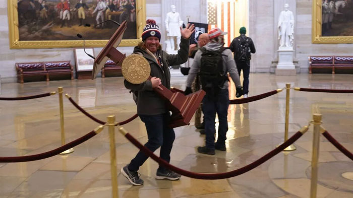 Man carrying a large object in a historic building, waving, with others nearby; a scene likely from a Florida Man headline.