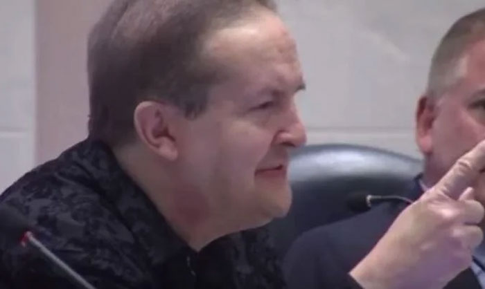 Man speaking at a meeting, gesturing with his hand, related to Florida Man headlines discussion.