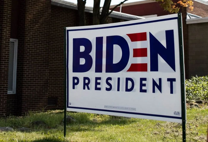 Campaign sign with "Biden President" in front of a brick building, showing support for a political candidate.