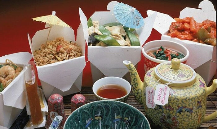 Chinese takeout boxes with colorful umbrellas, tea in a floral teapot, and a variety of dishes, representing Florida man cuisine.