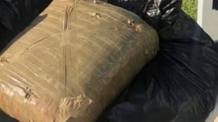 A large package wrapped in plastic, associated with Florida Man headlines, sits on a black trash bag.