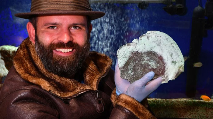 Man in a fur-lined jacket holding a fossil piece, showcasing a unique find by a Florida man in an aquarium setting.
