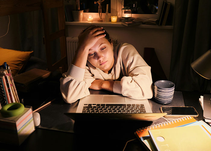 Woman looking tired at her laptop, managing time-off requests while saving PTO for vacations.