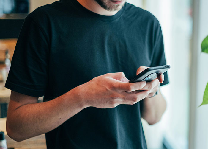 Man in black shirt using smartphone, related to manager saving workers&rsquo; PTO for vacations.