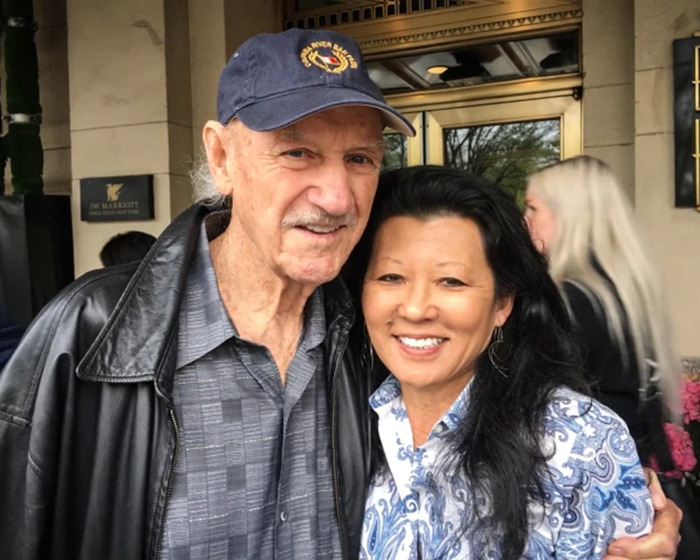 Smiling couple in casual attire outside a building; main keywords: Gene Hackman, family, autopsy results.