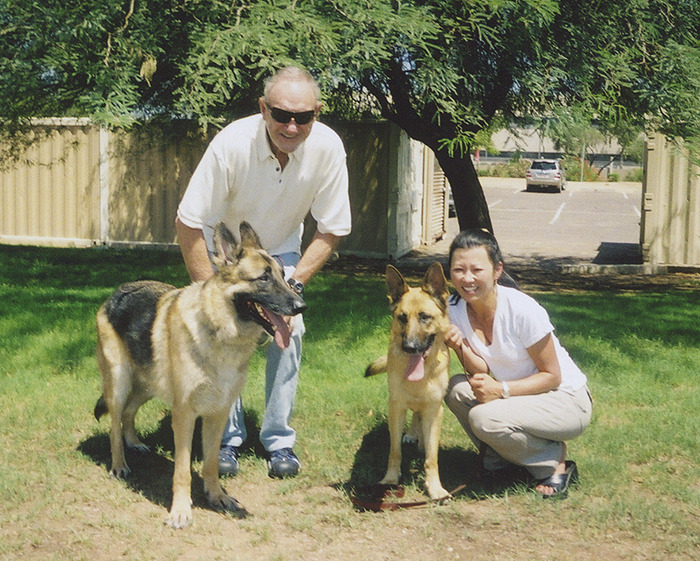 Man and woman with dogs in a sunny park setting, highlighting Gene Hackman's family keyword.