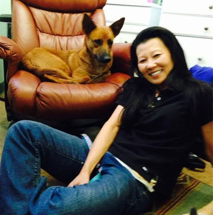 Smiling woman sitting on the floor beside a brown dog on a leather chair.