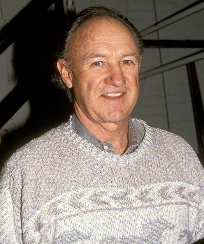 Gene Hackman in a sweater smiling at an event.