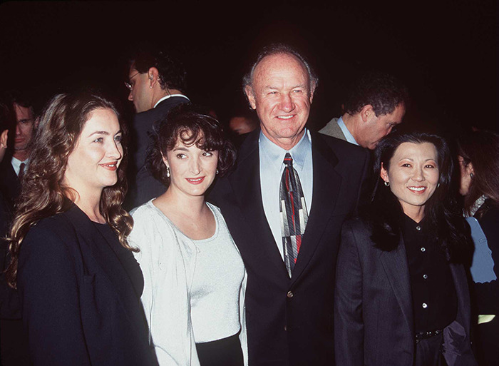 Gene Hackman smiling at an event, wearing a suit and patterned tie, with Betsy Arakawa and two kids in formal attire.