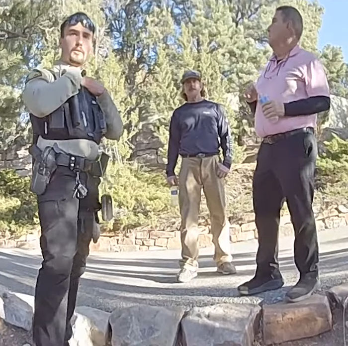 Police officer and two men in discussion outdoors, related to Gene Hackman complications.