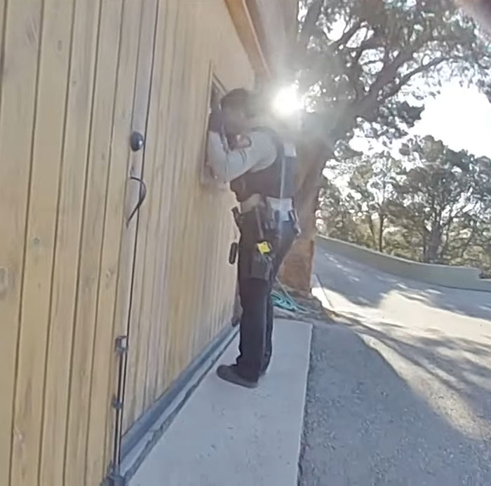 Officer inspects door during investigation after bodycam footage release, with sunlight in background.