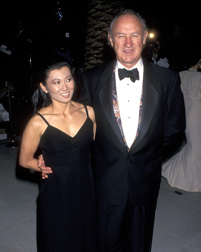 Gene Hackman and Betsy Arakawa in a black dress, poses with a man in formal attire at an event.
