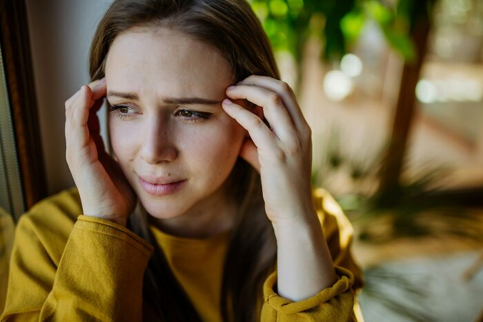 Woman in a yellow sweater looking distressed, reflecting on friendship issues near a window.