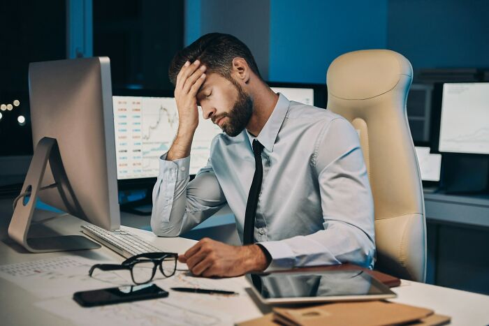 A frustrated office worker in a white shirt, seated at a desk with multiple screens, reflecting on a bad job bonus.