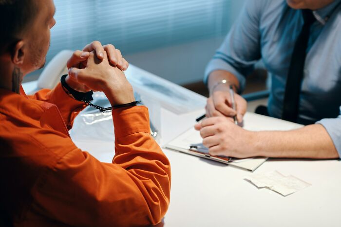 Therapist and client at a table, with client in handcuffs, discussing during a counseling session.