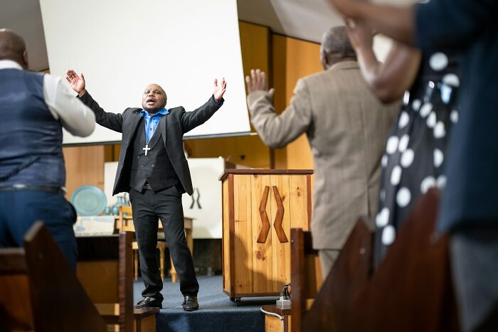 A preacher leading a church service passionately, gesturing with arms raised, focusing on secrets family members might keep.