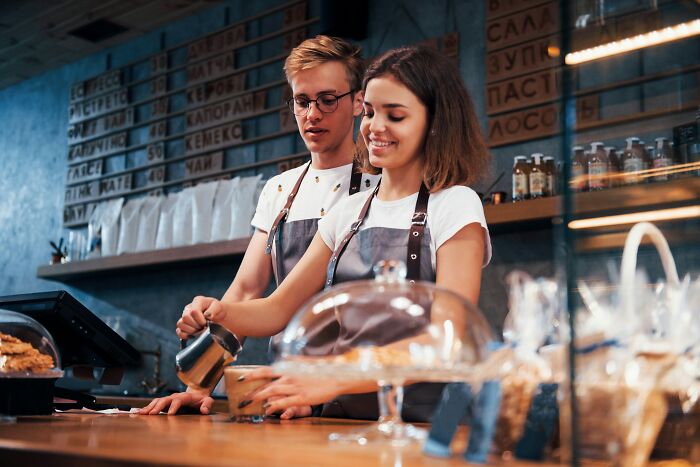 Two baristas working happily at a cafe counter, wearing aprons, representing life after "useless" degrees.