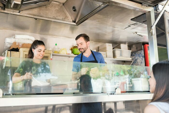 Couple cooking together in a food truck kitchen, wearing aprons.