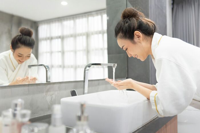 Woman washing hands at modern bathroom sink, illustrating inventions.