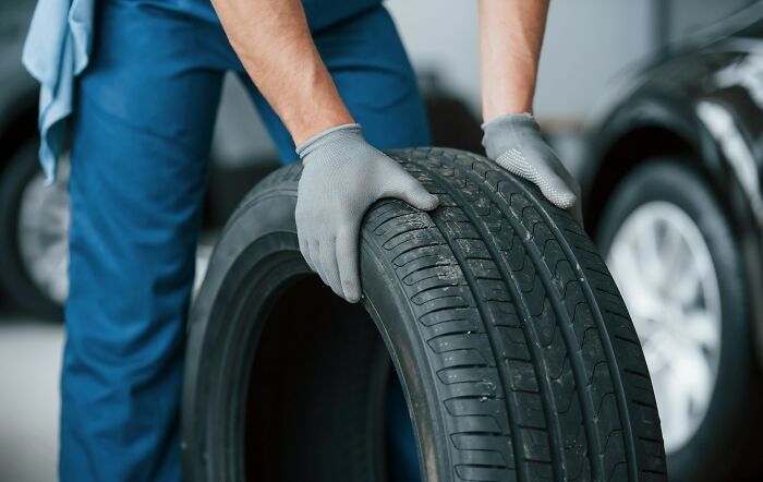 Person installing a car tire, illustrating a lifetime supply benefit in a garage setting.