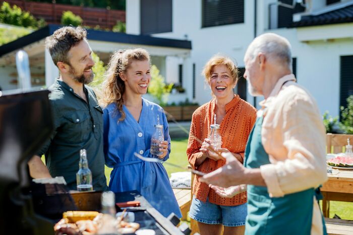 Four people happily chatting by a BBQ grill in a backyard gathering.