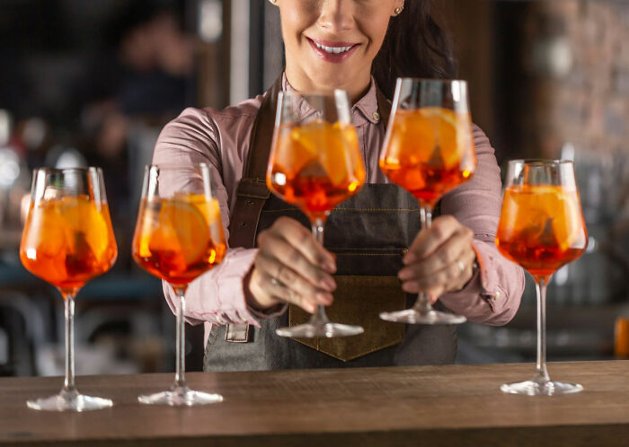Smiling bartender serving Aperol spritz cocktails, potential wedding red flag with vibrant orange drinks in glasses.