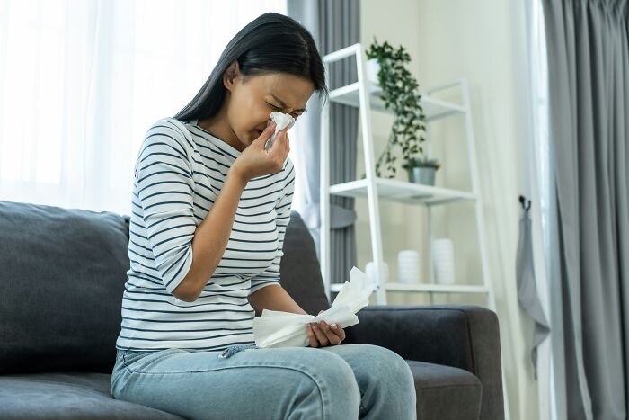 Woman on couch using tissues, possibly wishing for an invention for comfort.