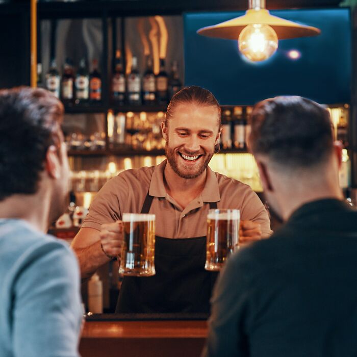 Bartender serving beer to two men at a wedding, highlighting potential red flags in a lively bar setting.