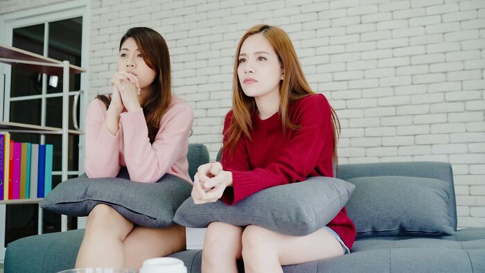 Two women sitting on a couch, looking pensive, highlighting reasons friendships with besties change over time.