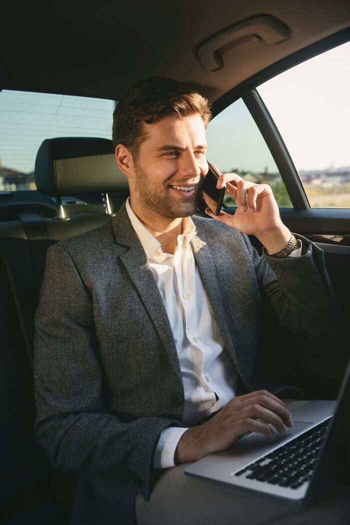 Man in a suit smiling, talking on the phone, and using a laptop in a car, highlighting easy ways to make money.