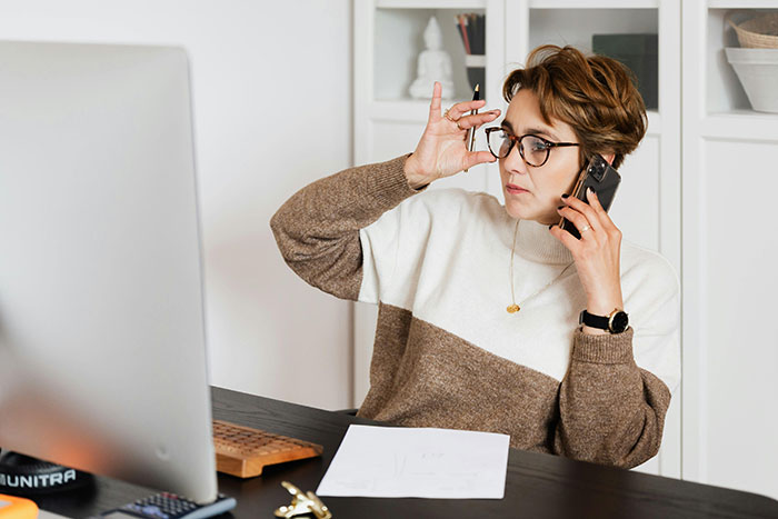 Woman in glasses at desk, holding phone, discussing body-shaming issues related to attention and self-worth.