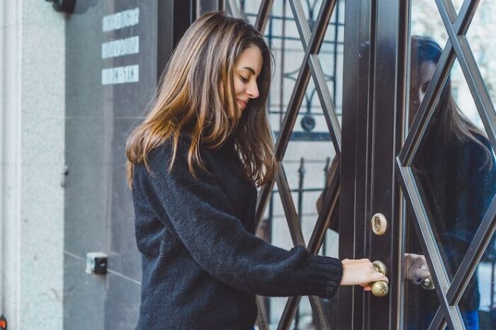 Woman in a black sweater opening a door, representing unsettling stories of crossing boundaries.