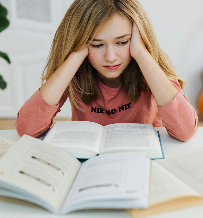 Girl looking stressed, sitting at a table with open books, symbolizing prioritizing family over plans with friends.