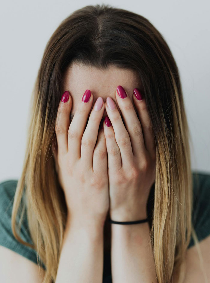 Person covering face with hands, upset over prioritizing family trip over plans with friends.